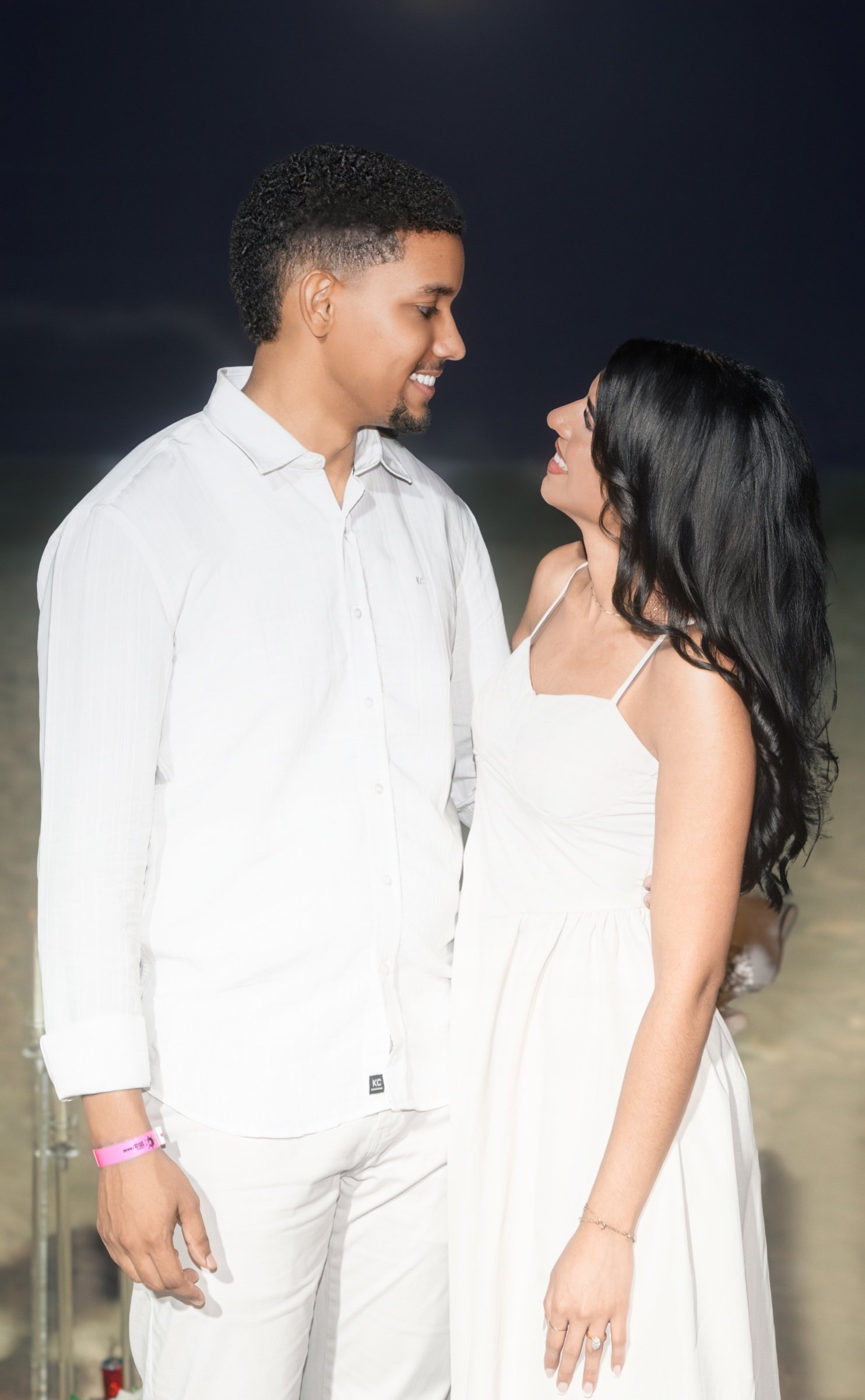 Moises y Sashalee se miran y sonríen, vestidos de blanco.